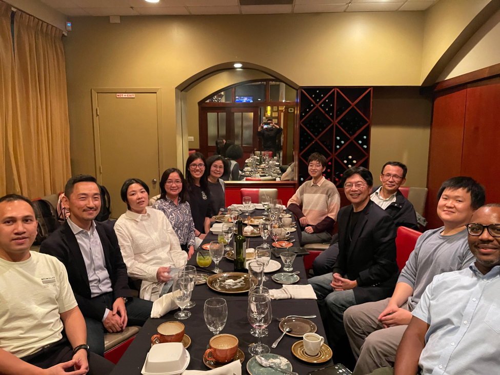 Phi sitting at a table at dinner with advisor Naoto T. Ueno, MD, PhD and labmates.
